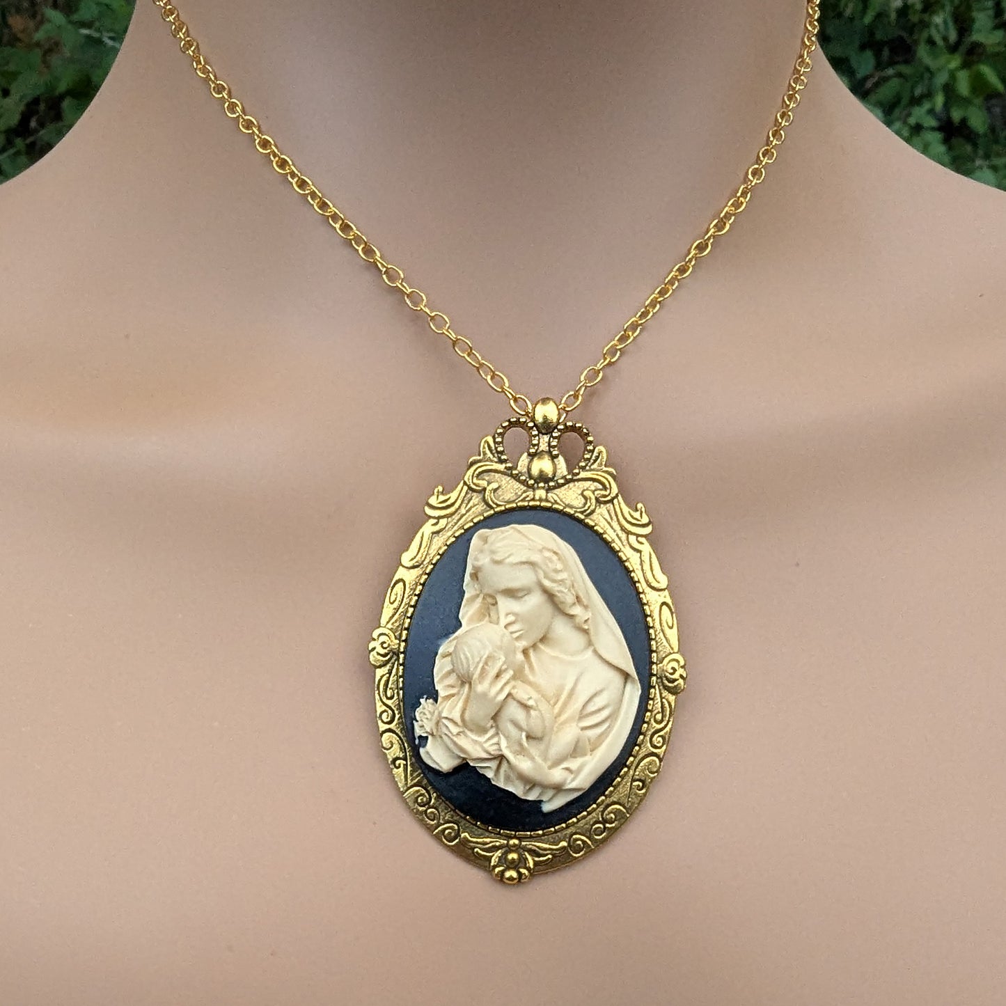Virgin Mother Mary Kissing the Head of Baby Jesus Cameo brooch pendant being worn with a chain around a neck