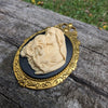 Virgin Mother Mary Kissing the Head of Baby Jesus Cameo brooch pendant resting on a log outside.