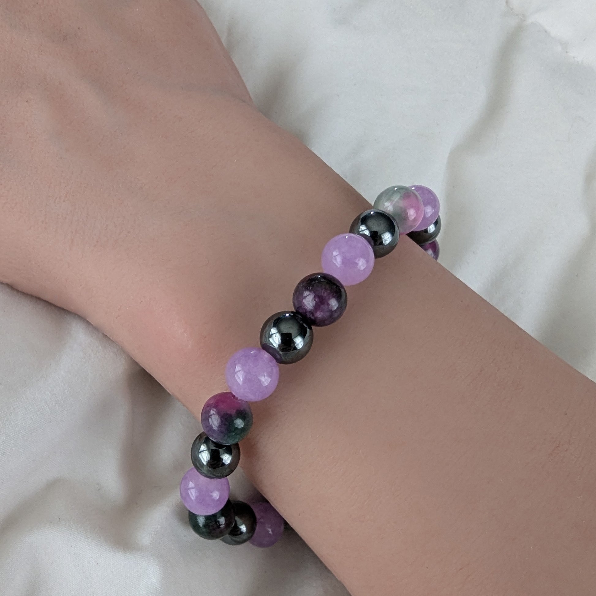 Bracelet with violet purple, Persian Jade and black hematite beads on a wrist against a white background