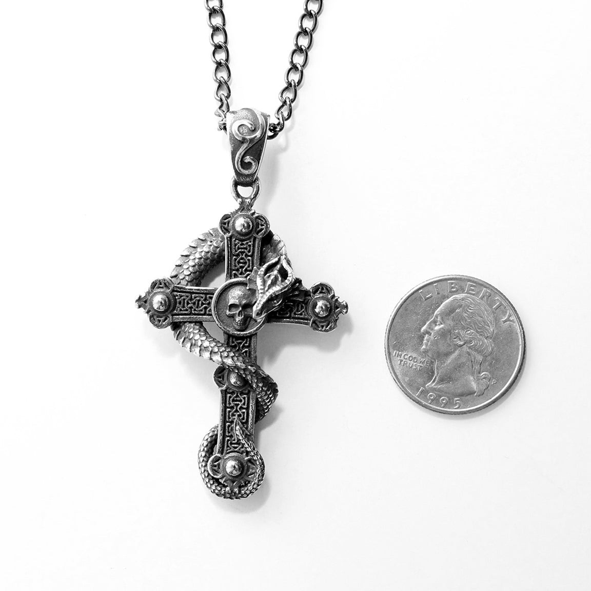 Silver cross pendant with intricate dragon and skull design on a white background with quarter for scale.  Gothic Fantasy Jewelry.