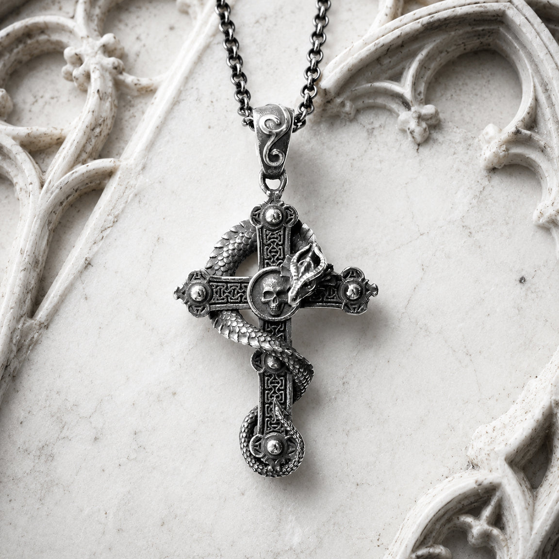 Decorative cross pendant necklace with a dragon and skull on a white stone surface.  Gothic Fantasy Jewelry.