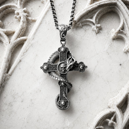 Decorative cross pendant necklace with a dragon and skull on a white stone surface.  Gothic Fantasy Jewelry.