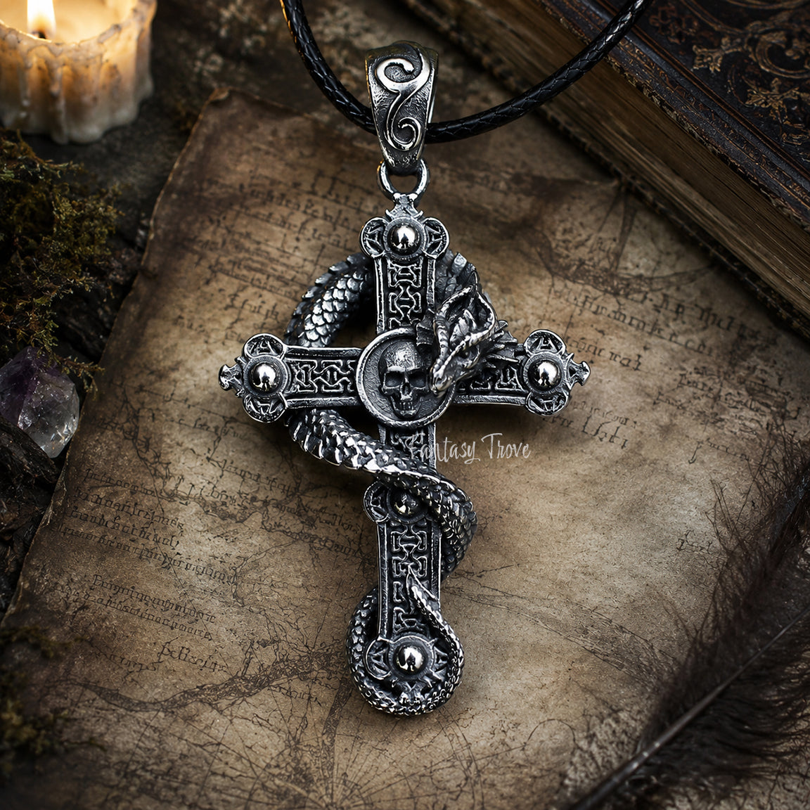 Silver cross pendant with intricate dragon and skull designs on an old book page.  Gothic Fantasy Jewelry.