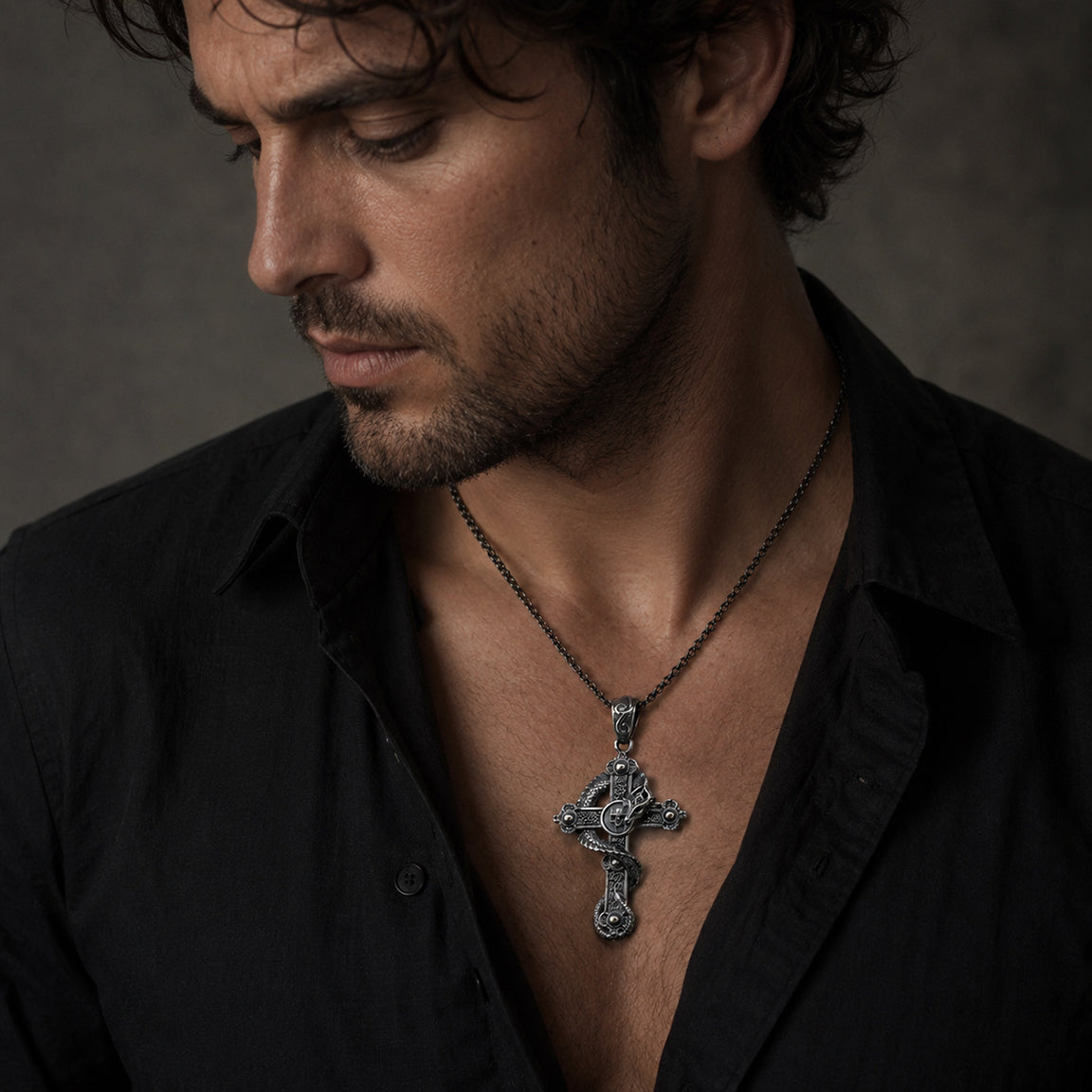 Man wearing a black shirt with an ornate cross necklace with a skull and dragon against a dark background.  Gothic fantasy biker jewelry