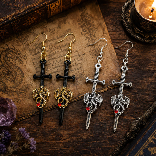 Pair of sword-shaped earrings with dragon designs on an old book with a candle and amethyst stone in the background.