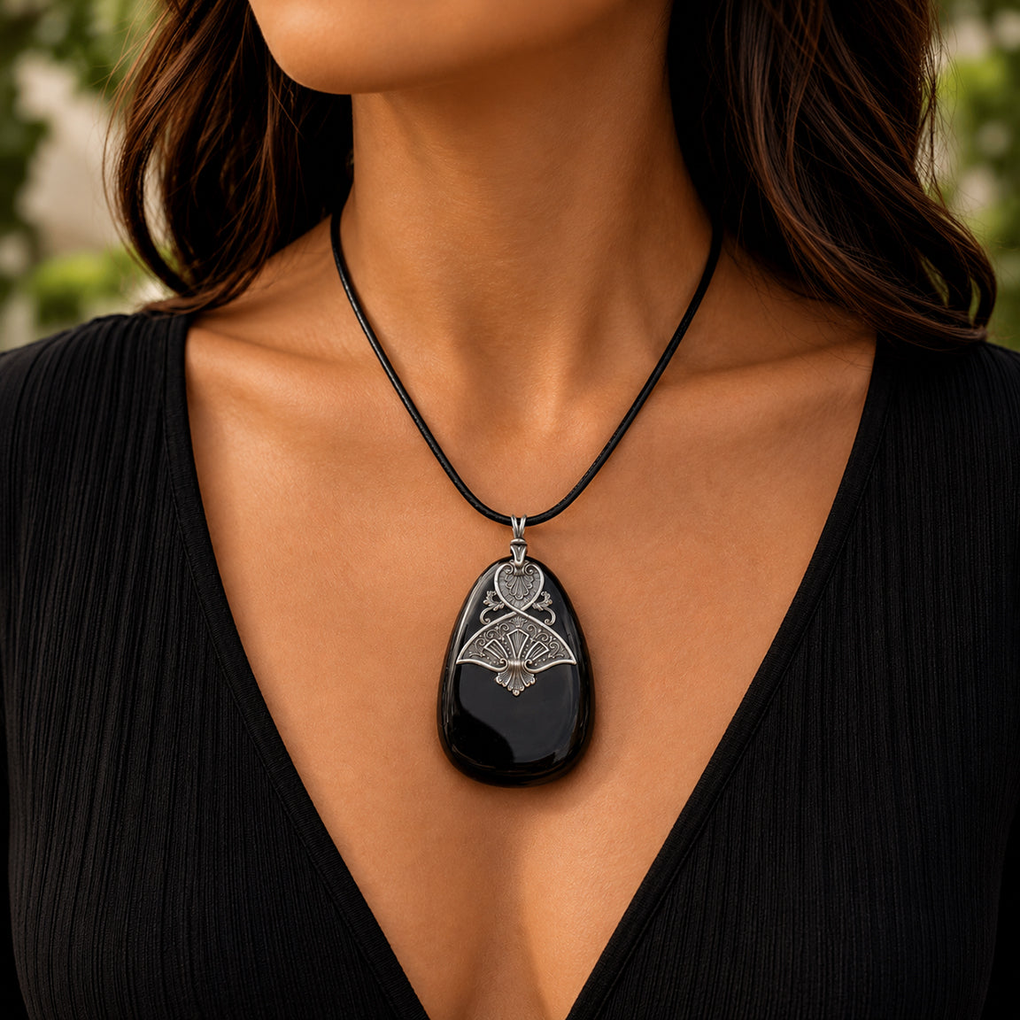 Black druzy pendant necklace on a person wearing a black top with a blurred natural background.  Gothic Egyptian inspired jewelry