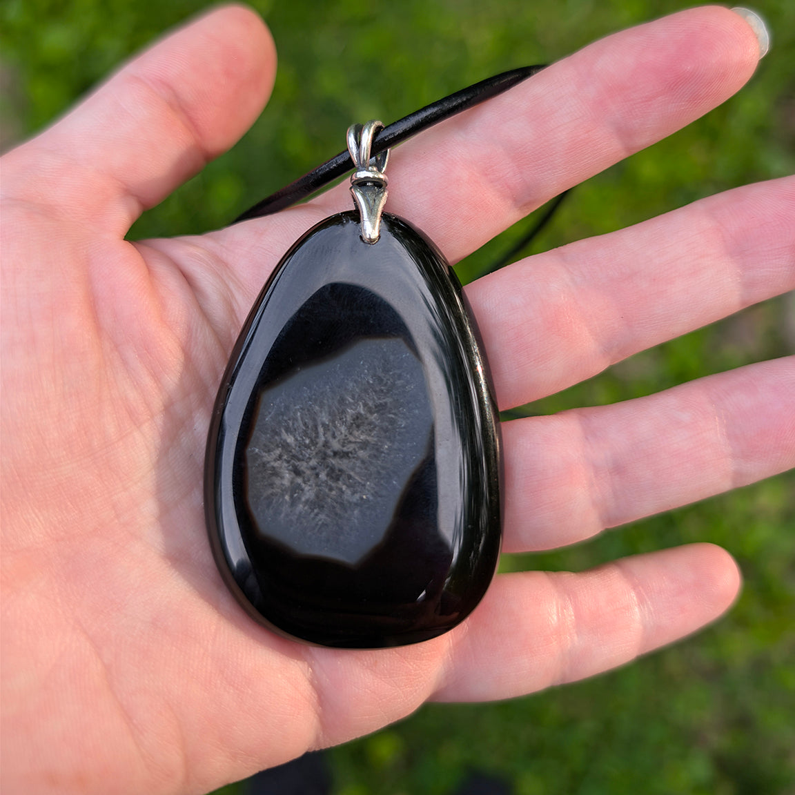 Black Druzy stone pendant held in a hand with a blurred green background