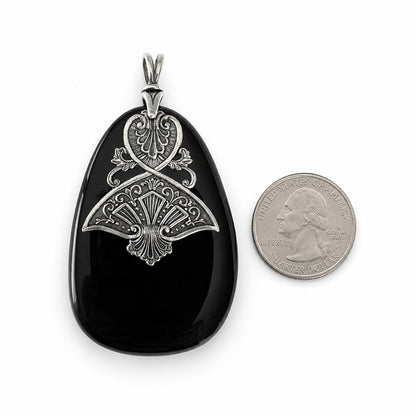 Black druzy stone pendant with silver intricate design next to a quarter for scale on a white background