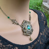 Ornate necklace with green gemstones worn by a person in a black lace top, outdoor setting.