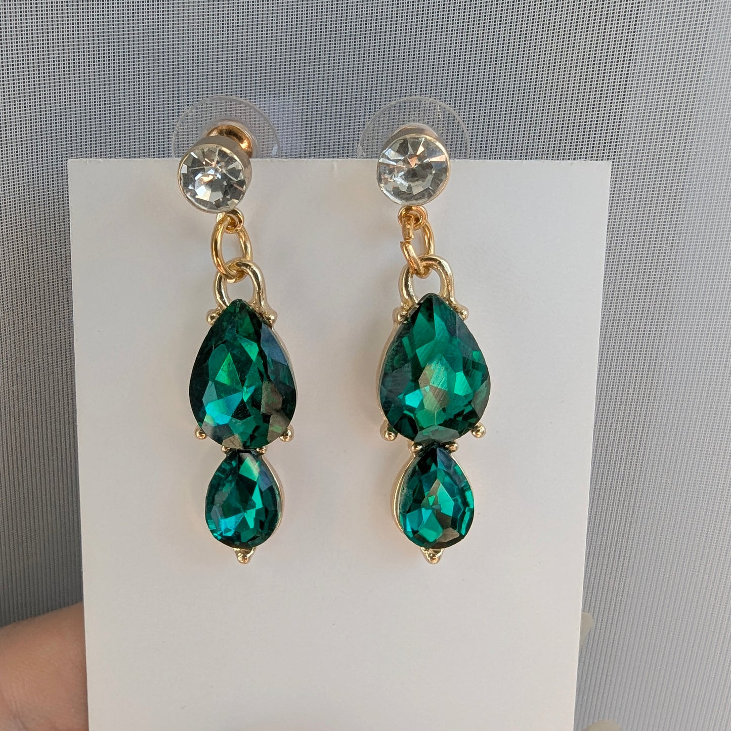 Green teardrop earrings with gold accents on a white card against a gray background