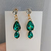 Green teardrop earrings with gold accents on a white card against a gray background