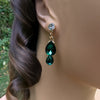 Green teardrop earrings worn by a person with a blurred natural background