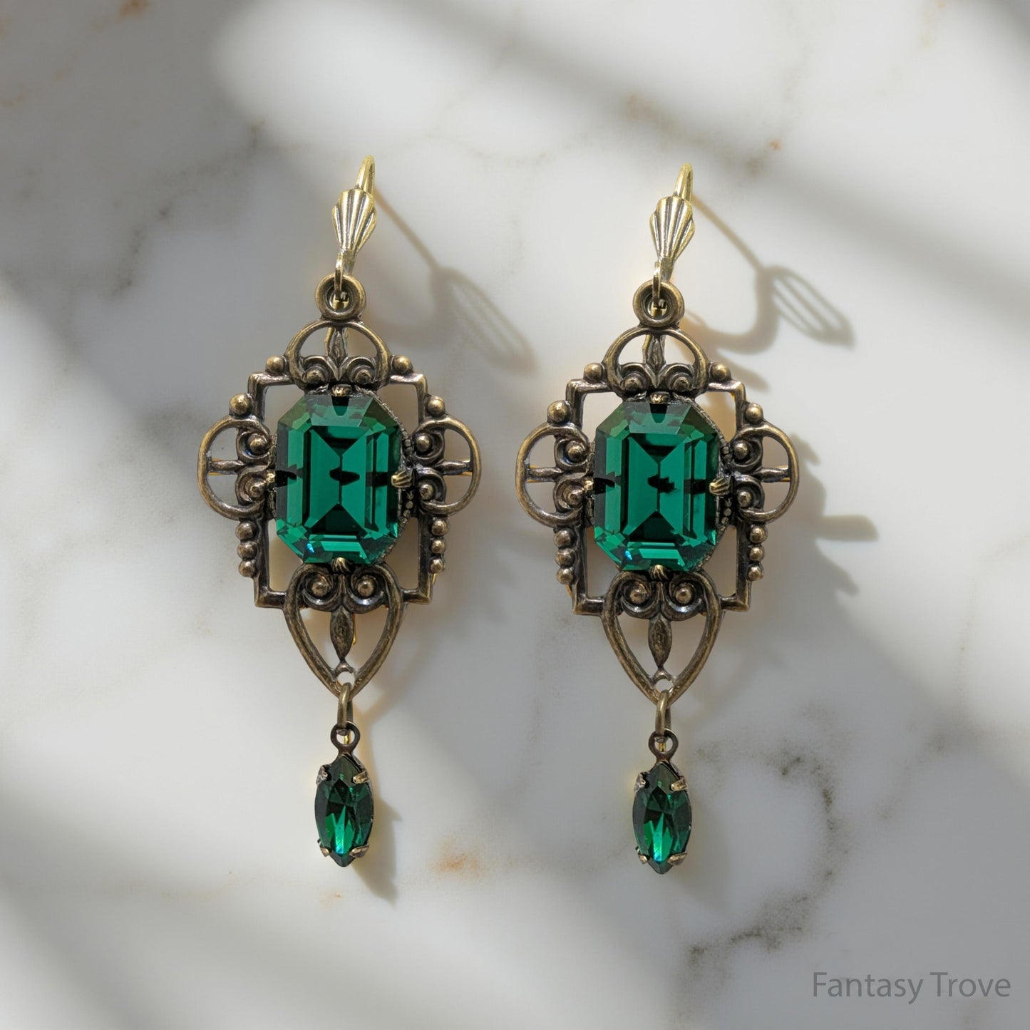 Pair of ornate earrings with green gemstones on a marble surface