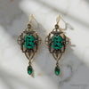 Pair of ornate earrings with green gemstones on a marble surface
