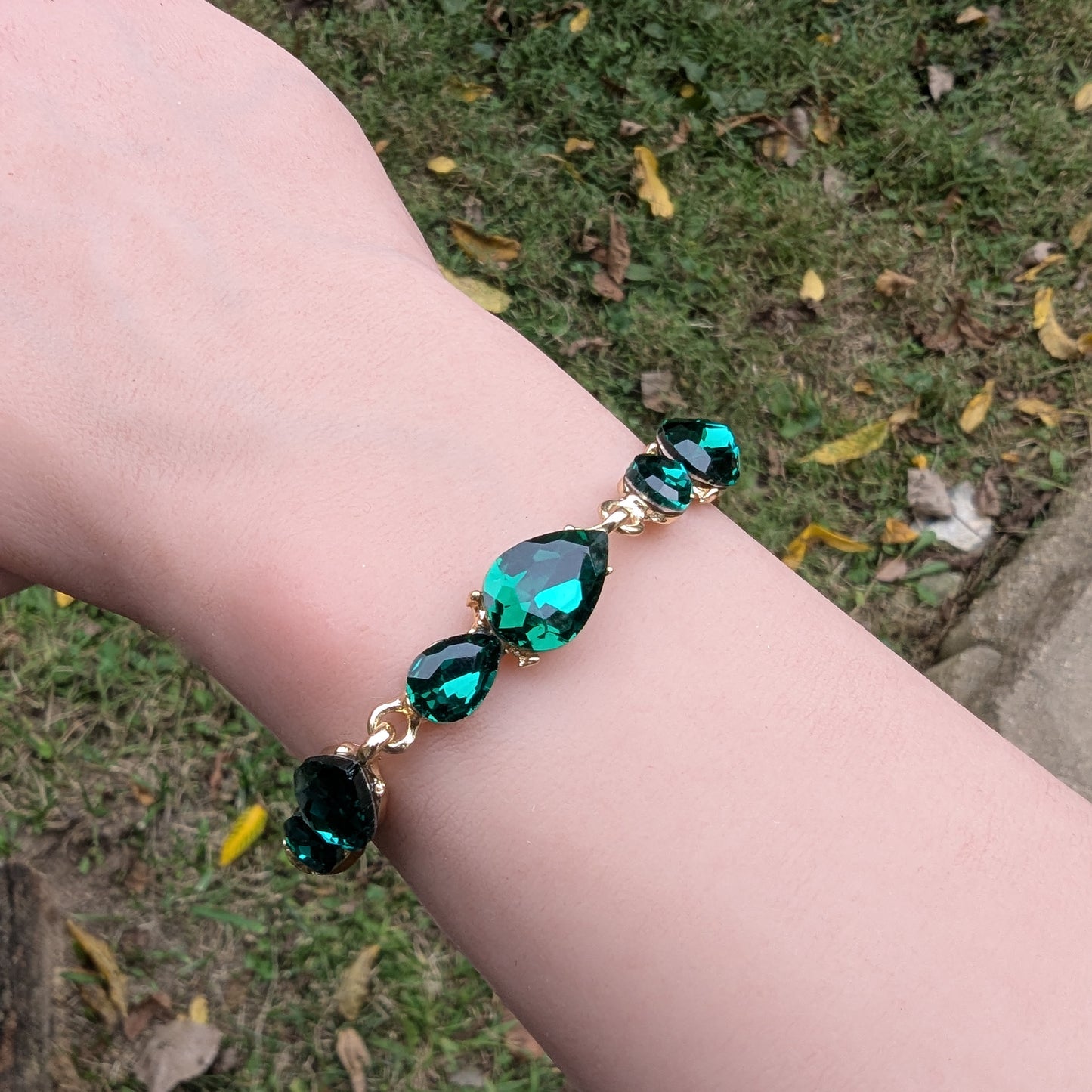 Bracelet with emerald green gemstones on a wrist against a grassy background