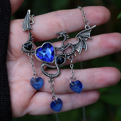 Hand holding a silver dragon pendant with blue heart gemstones against a blurred green background.  Gothic romance dragon fantasy jewelry.