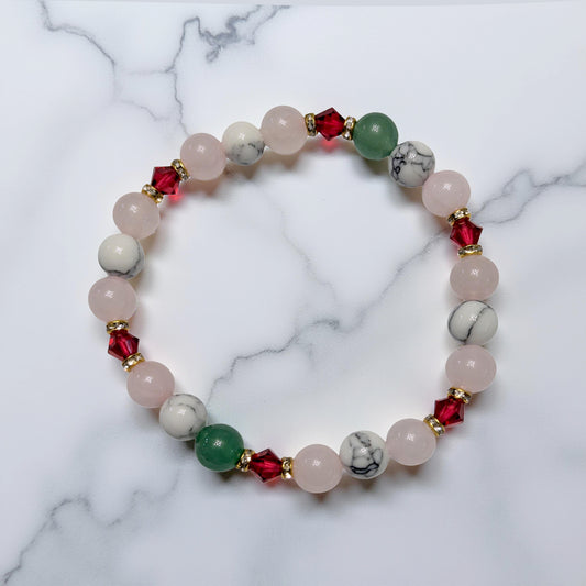 Holiday beaded natural stone stretch bracelet made with rose quartz, green aventurine and white howlite beads, accented by red Swarovski crystals on white marble surface