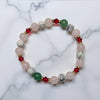 Holiday beaded natural stone stretch bracelet made with rose quartz, green aventurine and white howlite beads, accented by red Swarovski crystals on white marble surface