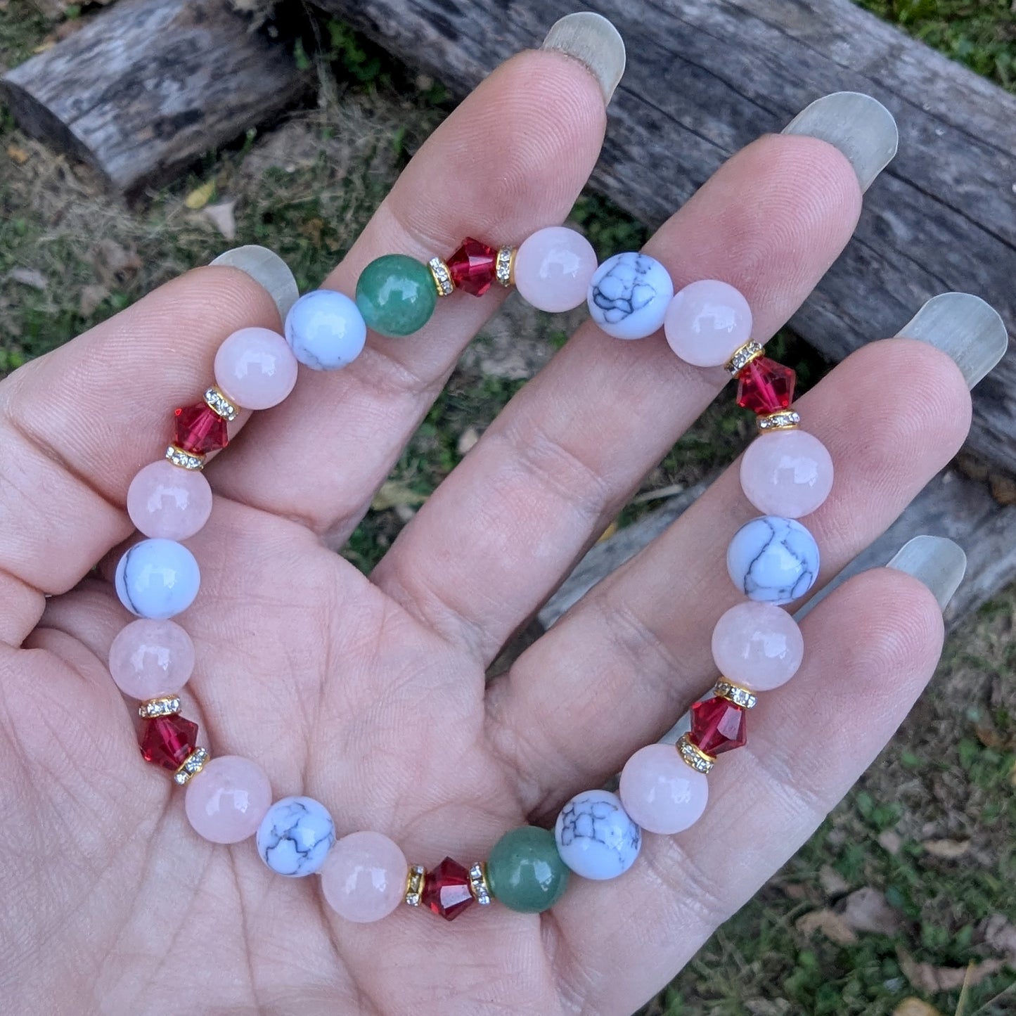Hand holding a Holiday beaded natural stone stretch bracelet made with rose quartz, green aventurine and white howlite beads, accented by red Swarovski crystals 