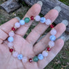 Hand holding a Holiday beaded natural stone stretch bracelet made with rose quartz, green aventurine and white howlite beads, accented by red Swarovski crystals 