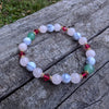 Holiday beaded natural stone stretch bracelet made with rose quartz, green aventurine and white howlite beads, accented by red Swarovski crystals on a wooden surface