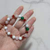 Hand holding a beaded bracelet with white, green, and red beads on a marble surface