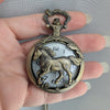 Bronze pocket watch with horse design held in a hand against a neutral background