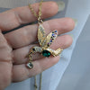 Gold hummingbird pendant necklace held in a hand against a neutral background