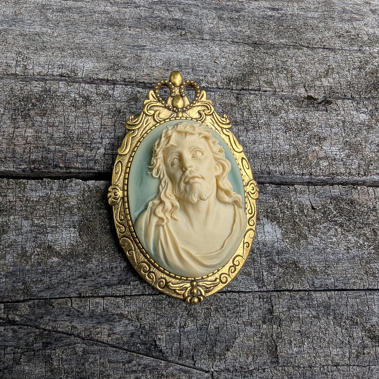 Gold-framed pendant with a 3D portrait of Jesus on a wooden surface