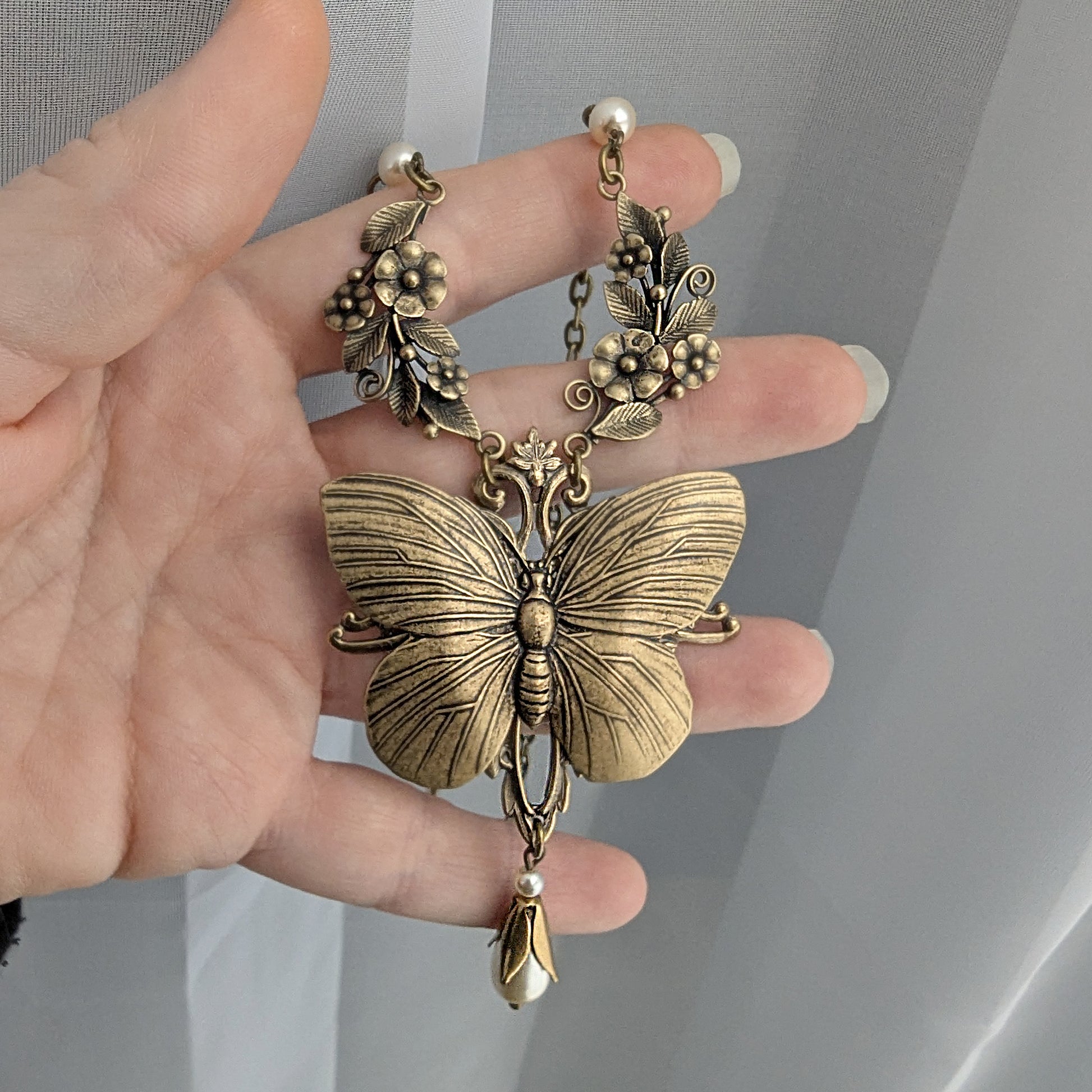 Brass Vintage Butterfly-shaped pendant held by a hand against a neutral background