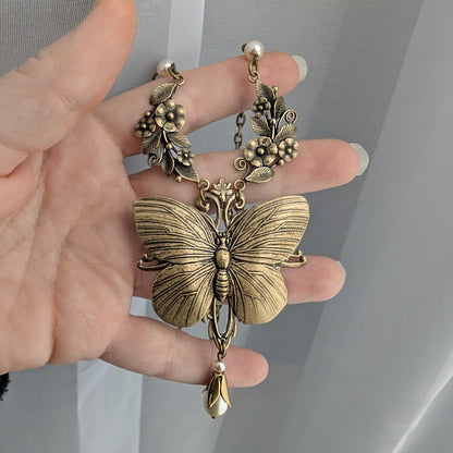 Brass Vintage Butterfly-shaped pendant held by a hand against a neutral background