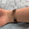 Bracelet with brown leather strap and copper accents on a wrist against a light gray background