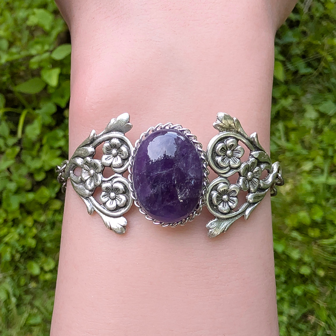Silver bracelet with an Amethyst gemstone worn on a wrist against a grassy background