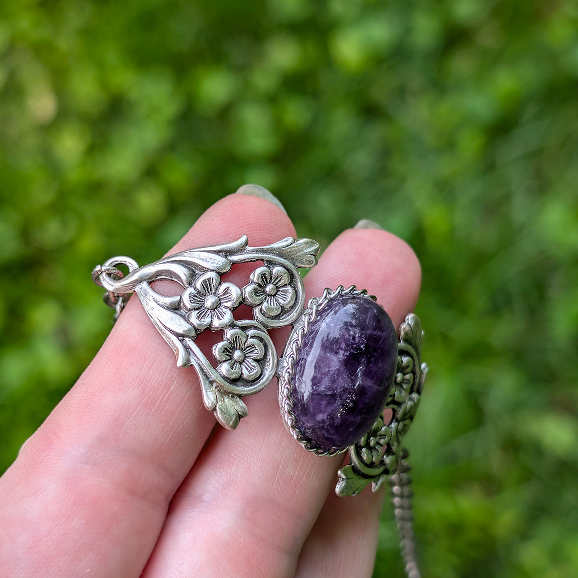 Hand holding a Vintage Amethyst Bracelet with Floral Detail against a green blurred background.