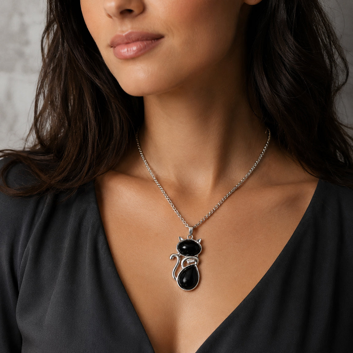 Woman wearing a necklace with a black onyx cat  pendant against a neutral background.  Cat lover jewelry gift.