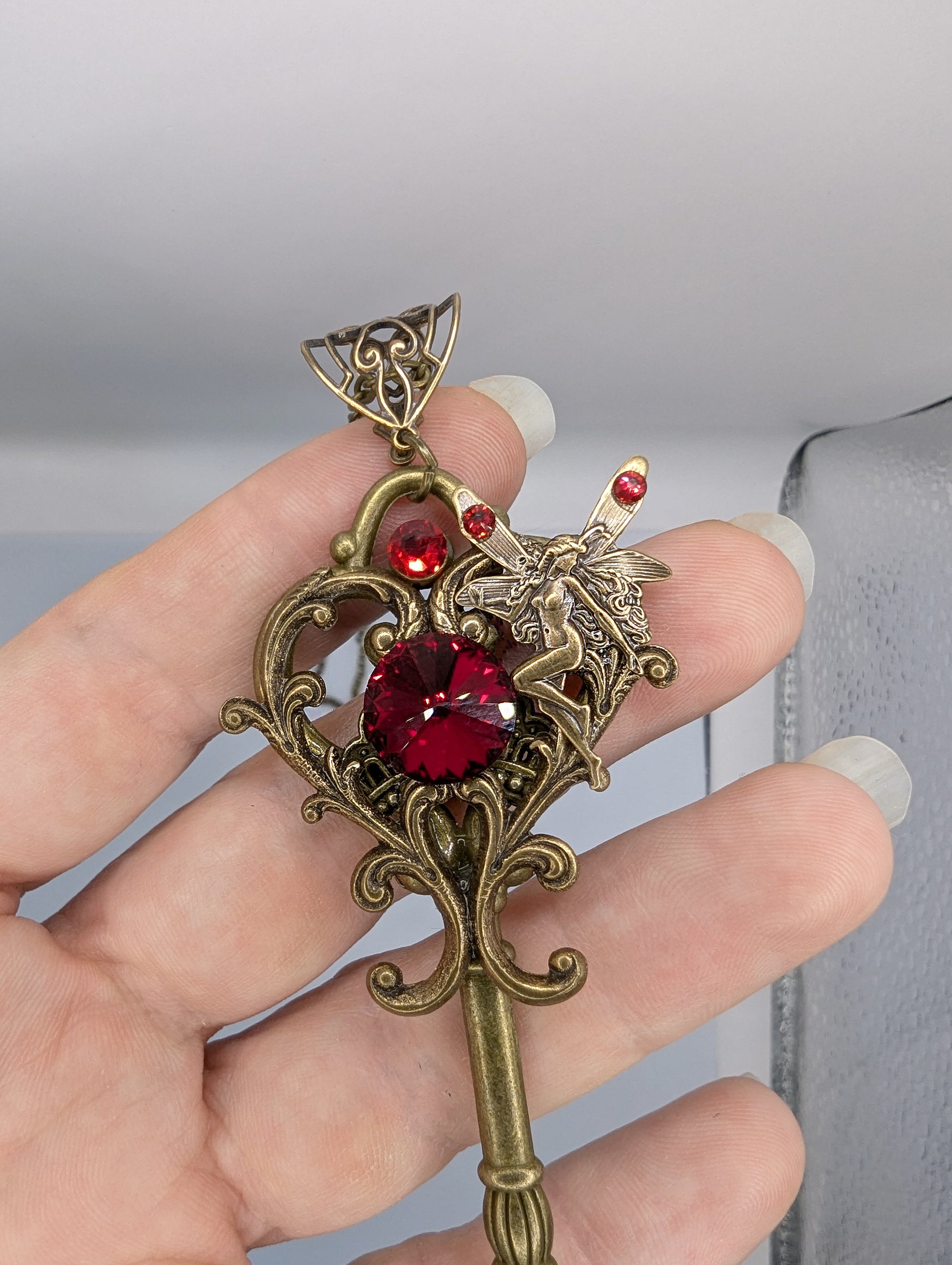 Decorative key-shaped pendant with red gemstones held in a hand against a neutral background