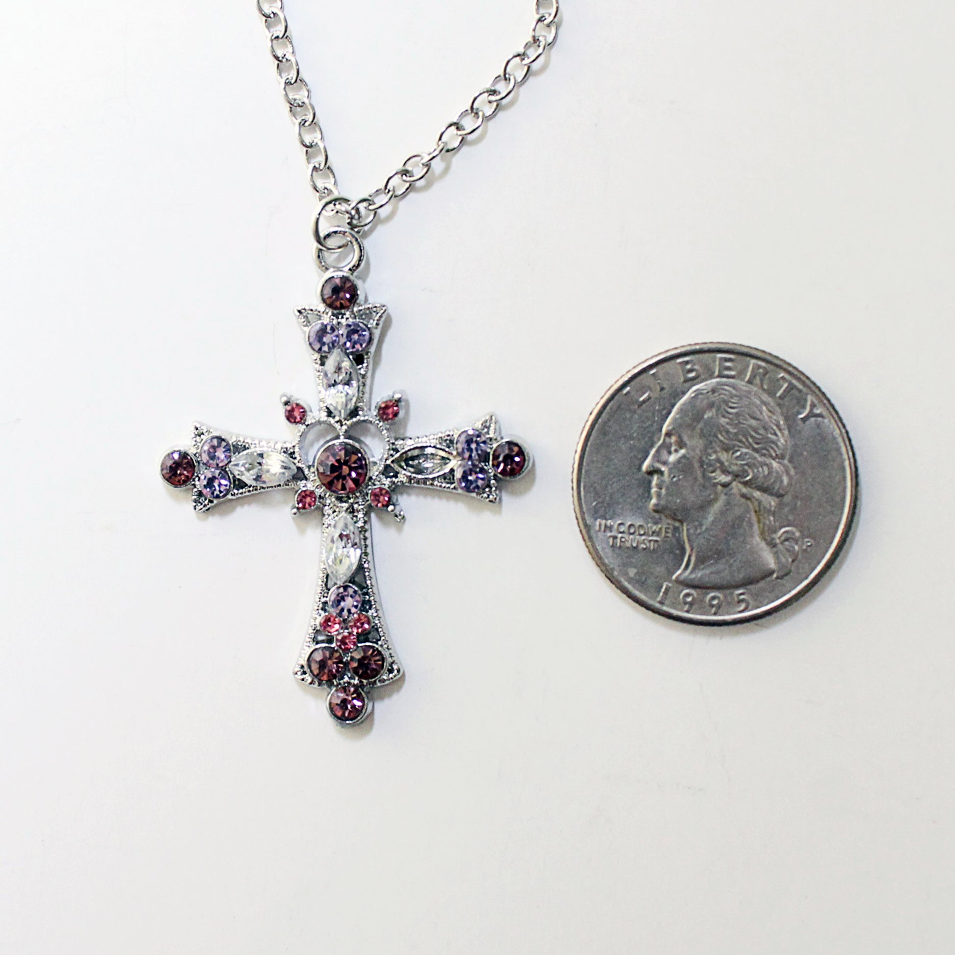 Silver cross necklace with pink and purple crystals next to a quarter on a white background