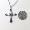 Silver cross necklace with pink and purple crystals next to a quarter on a white background