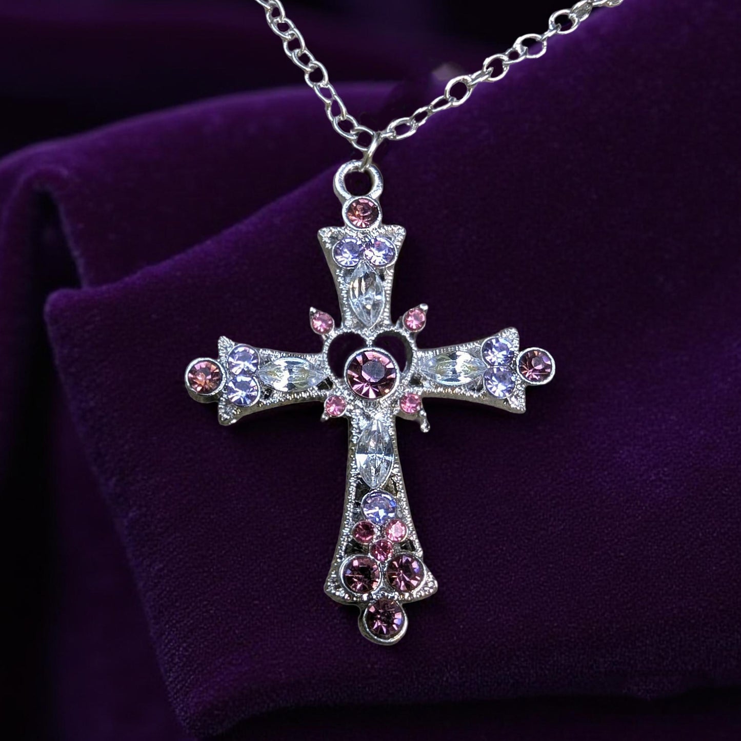 Decorative cross necklace with pink , purple and clear stones on a purple background
