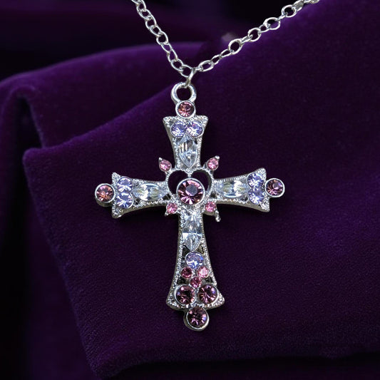 Decorative cross necklace with pink , purple and clear stones on a purple background