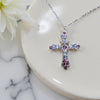 Silver cross necklace with pink and purple stones on a marble surface with a white flower.