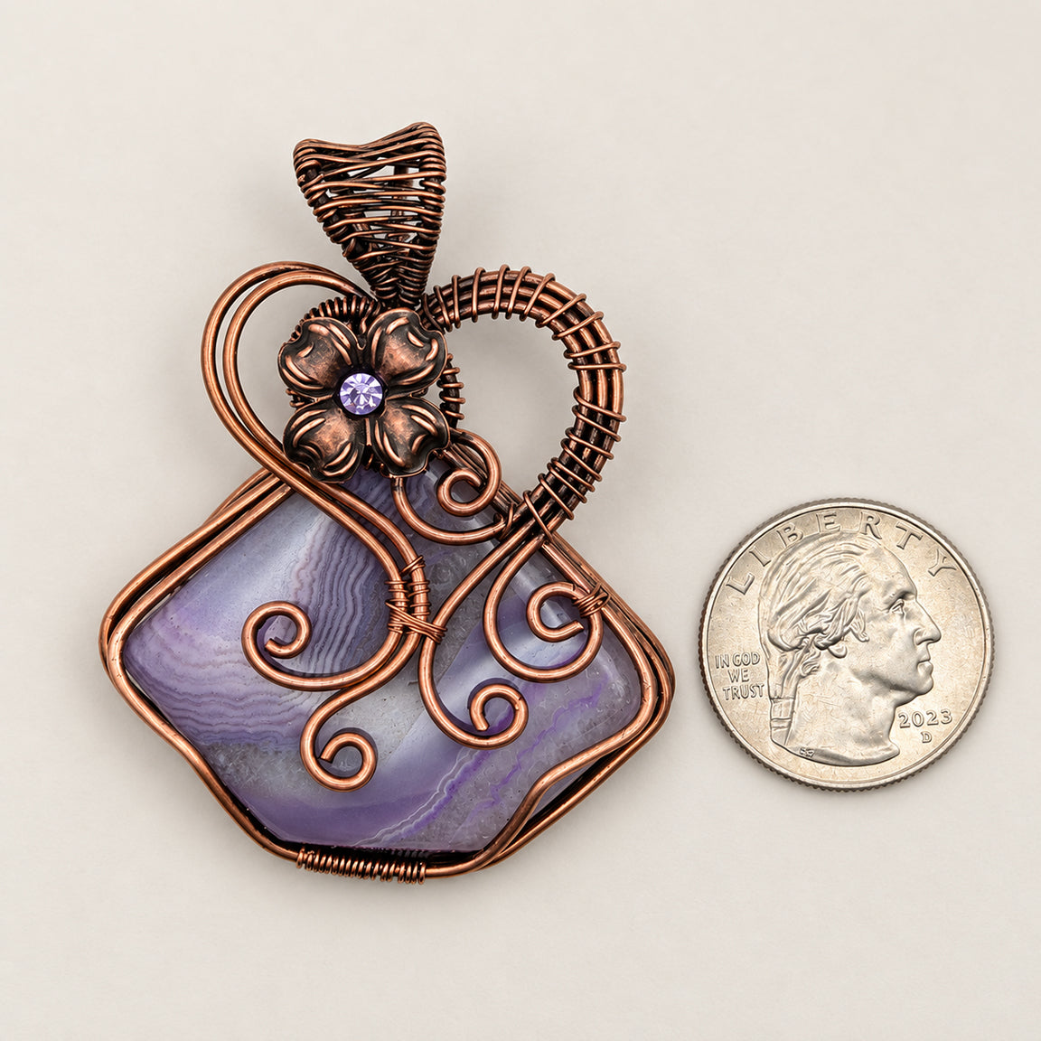 Wire wrapped purple solar agate fairy pendant with flower next to a U.S. quarter