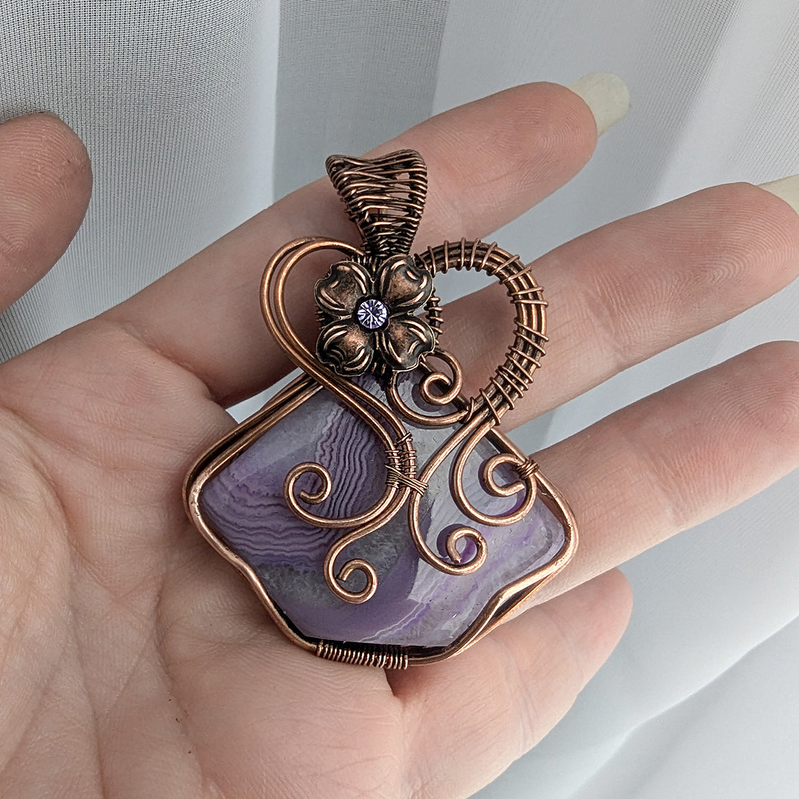 Wire wrapped purple solar agate fairy pendant with flower held in a hand
