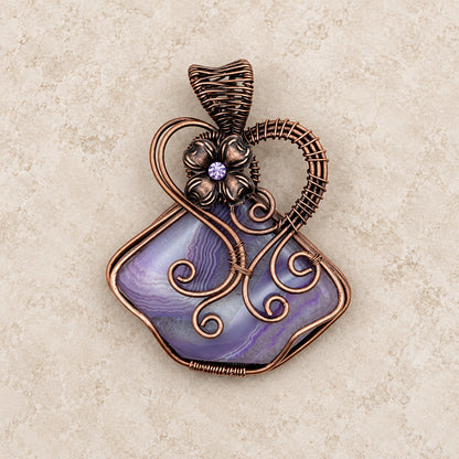 Wire wrapped purple solar agate fairy pendant with flower on a neutral background