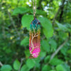 Colorful crystal pendant necklace with a green, blue, and pink design against a blurred green leafy background.