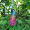 rainbow quartz crystal pendant on a chain against a green leafy background