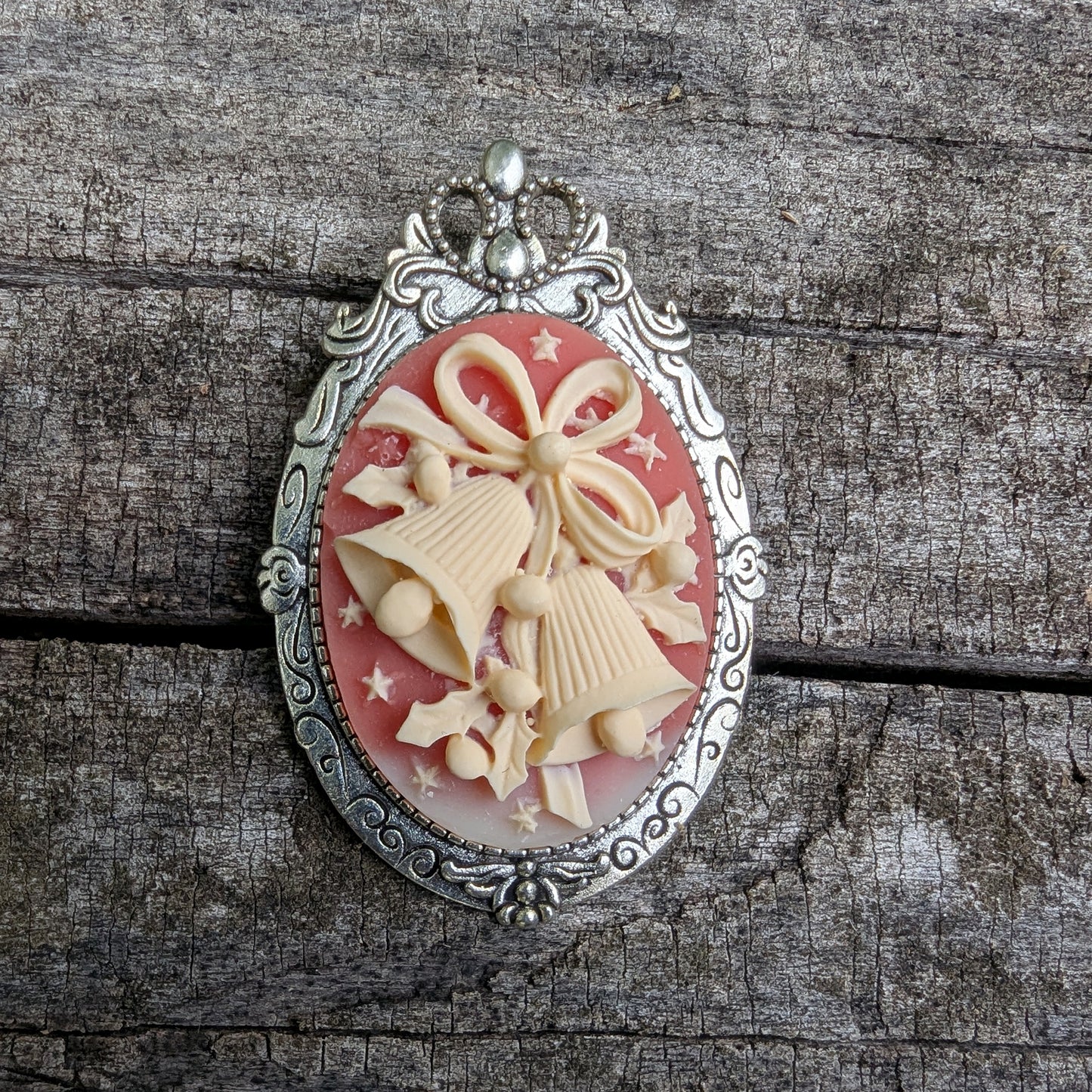  Pendant and brooch combo with decorative cream colored holiday bells on red background and silver frame on wood surface