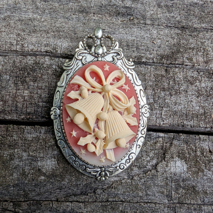  Pendant and brooch combo with decorative cream colored holiday bells on red background and silver frame on wood surface