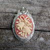  Pendant and brooch combo with decorative cream colored holiday bells on red background and silver frame on wood surface