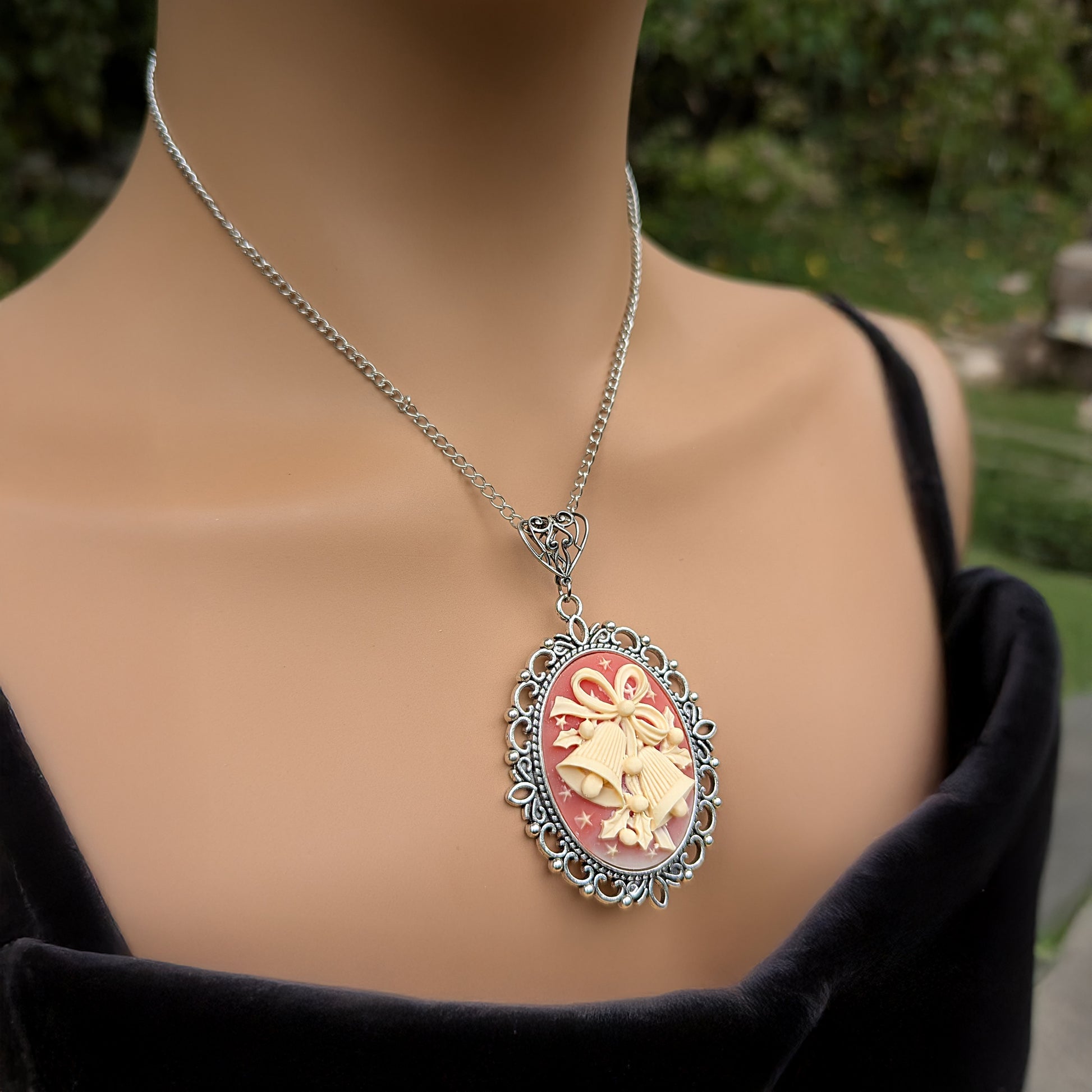 Necklace Pendant with decorative cream colored holiday bells on red background and silver frame being worn by model